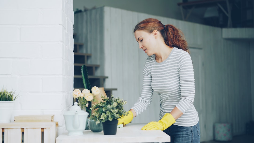 A cheerful young maid is wiping down the furniture with a damp cloth in a bright, modern apartment. Housework, people and interiors concept.